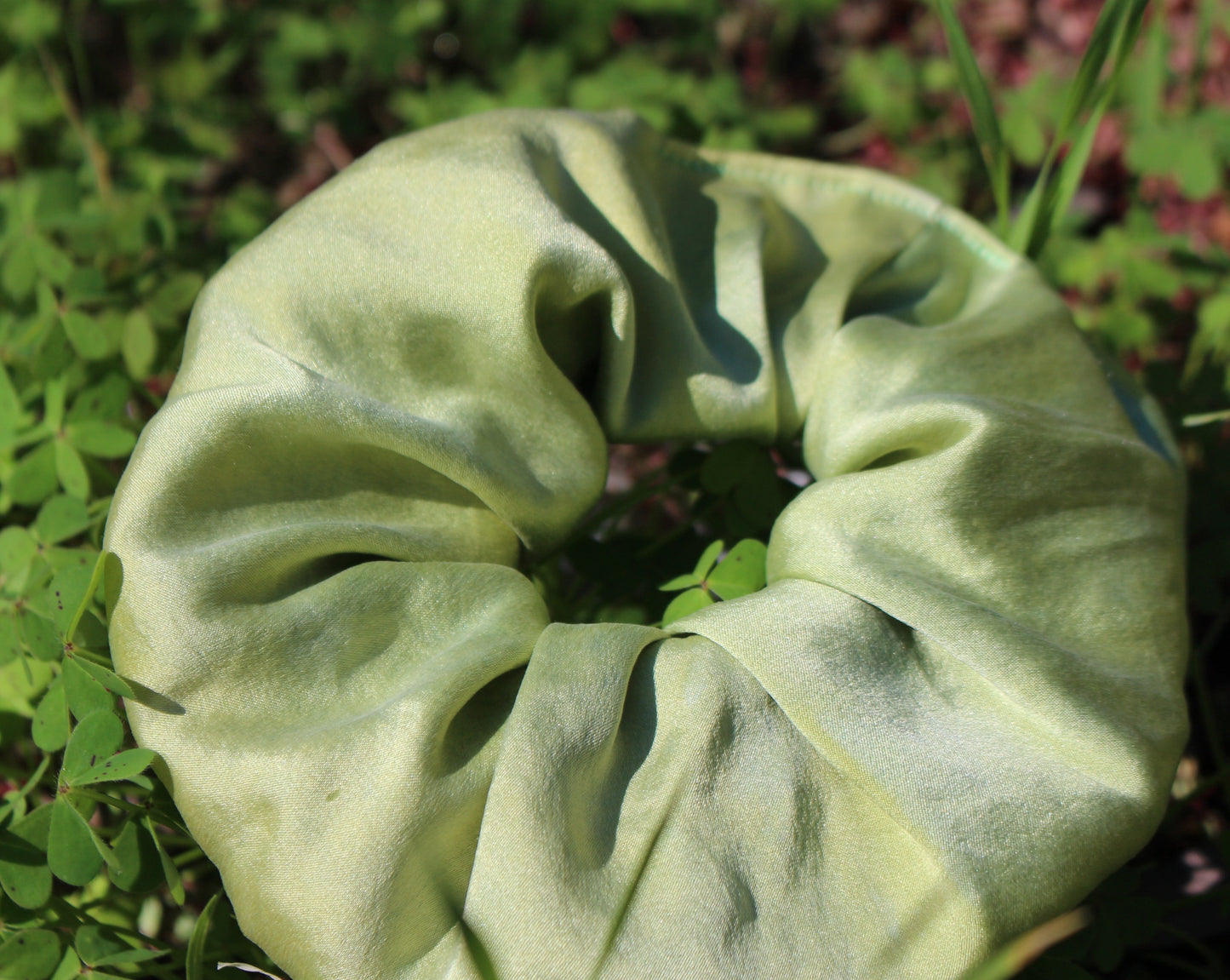 Mint green silk plant dyed scrunchie laying in the grass