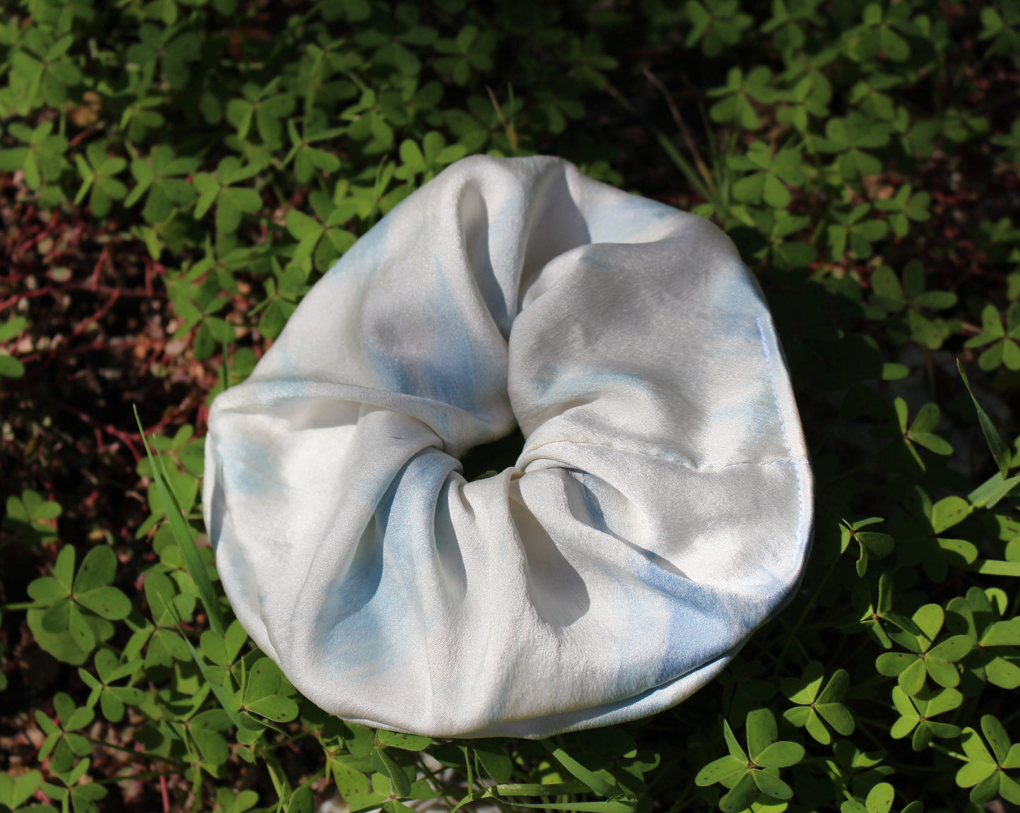 Tie dyed indigo blue and white silk scrunchie lying in a bed of clovers