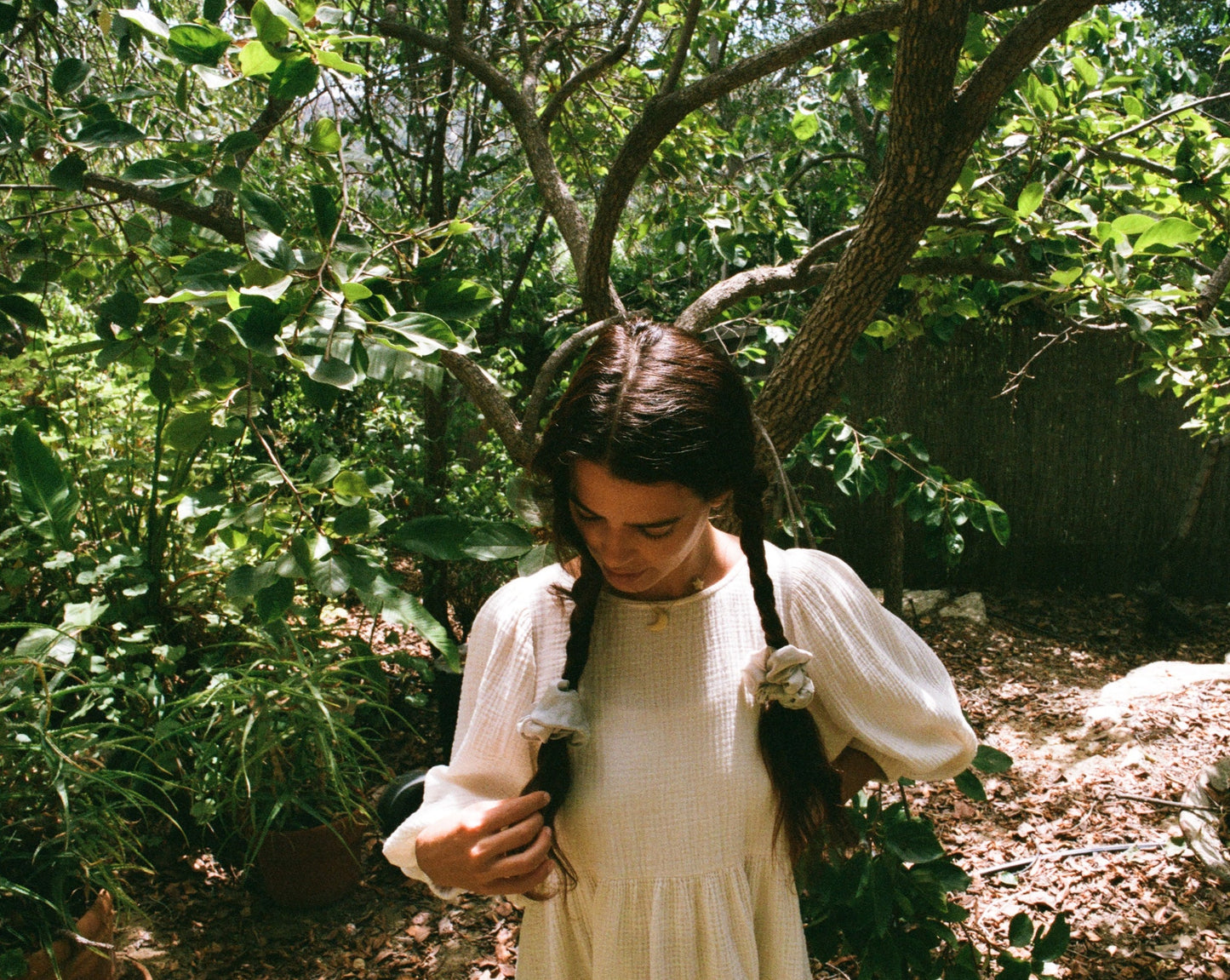 Woman looking down at her dark brown hair tied in braids. She has light blue silk scrunchies naturally dyed with sustainable indigo by Goose Summer.