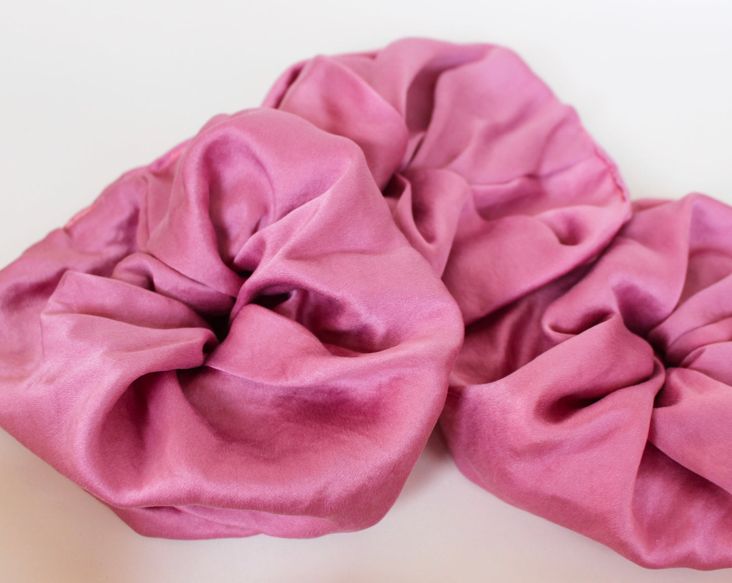 Goose Summer is a small, sustainable plant dyeing business making naturally dyed silk scrunchies and other accessories in Los Angeles. Three fuchsia colored plant dyed silk scrunchies made by Goose Summer.