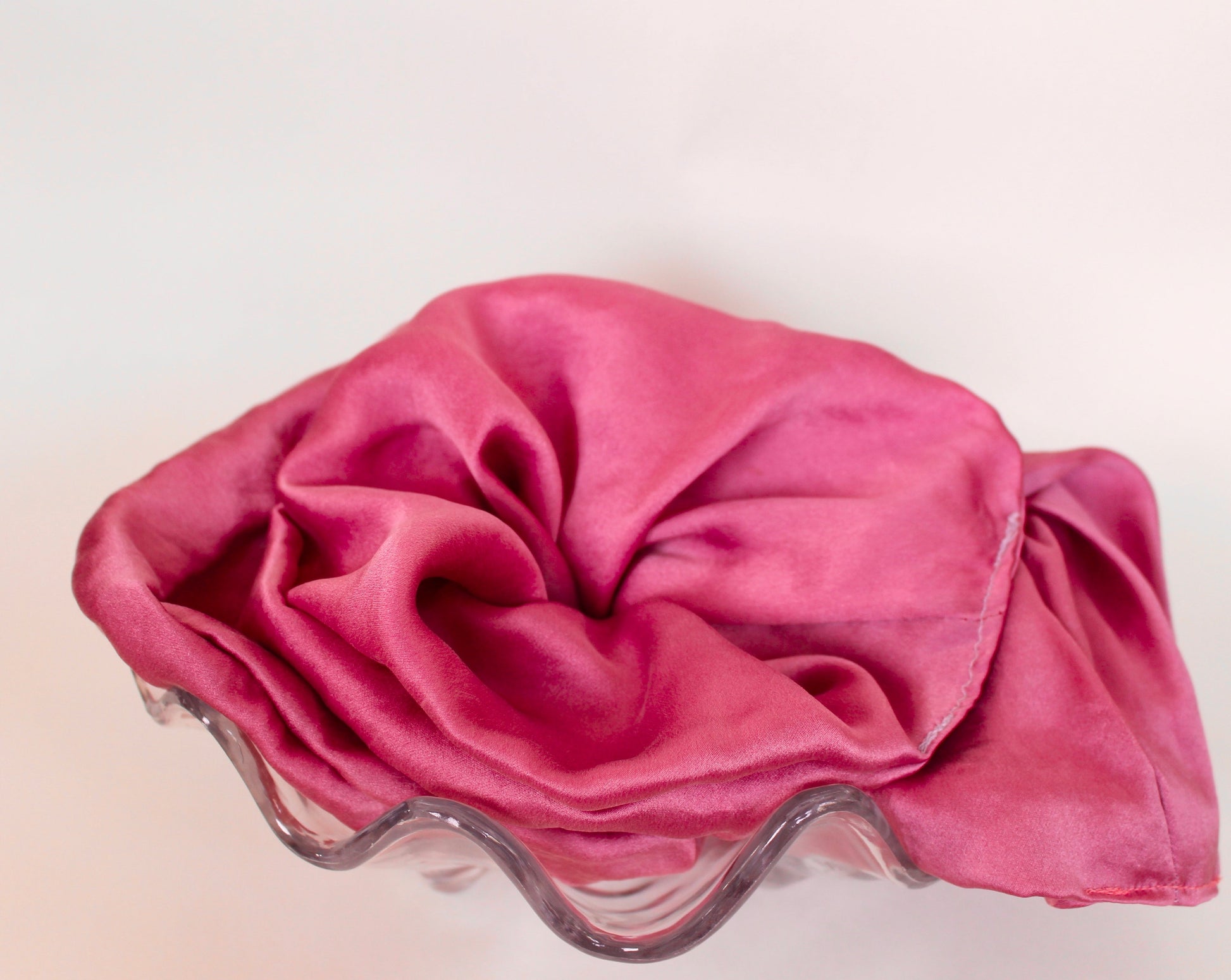 Goose Summer is a small, sustainable plant dyeing business making naturally dyed silk scrunchies and other accessories in Los Angeles. Two fuchsia plant dyed silk scrunchies displayed in a glass seashell bowl.