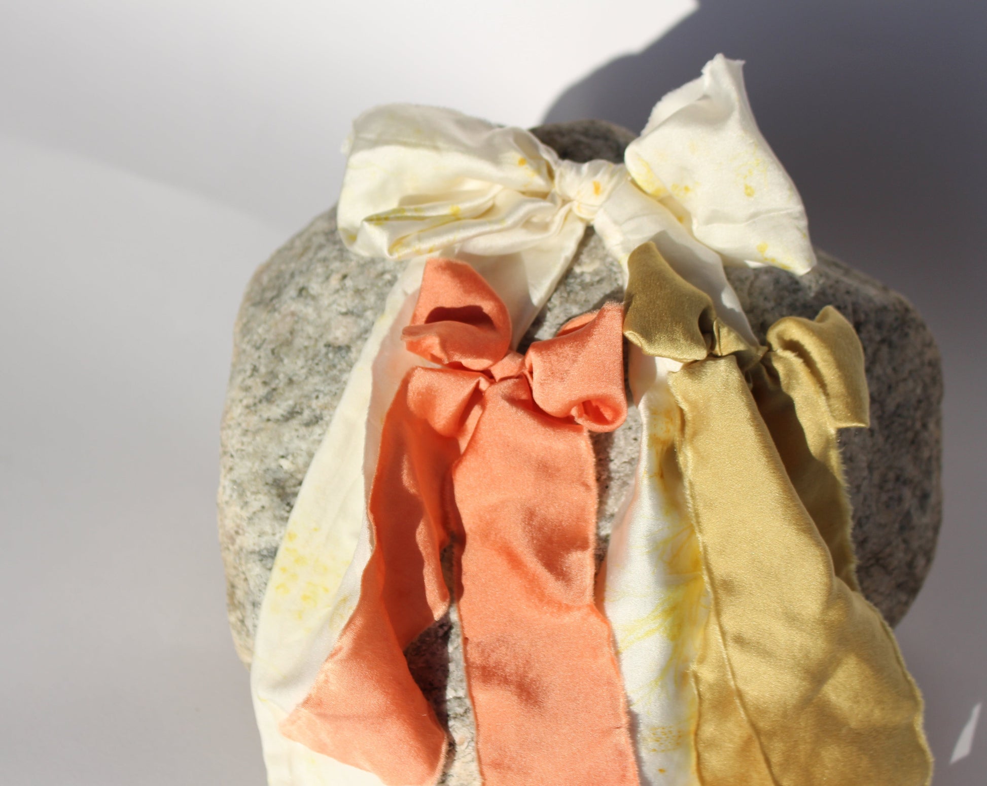 White, peach and green silk plant dyed bows laying flat on a rock