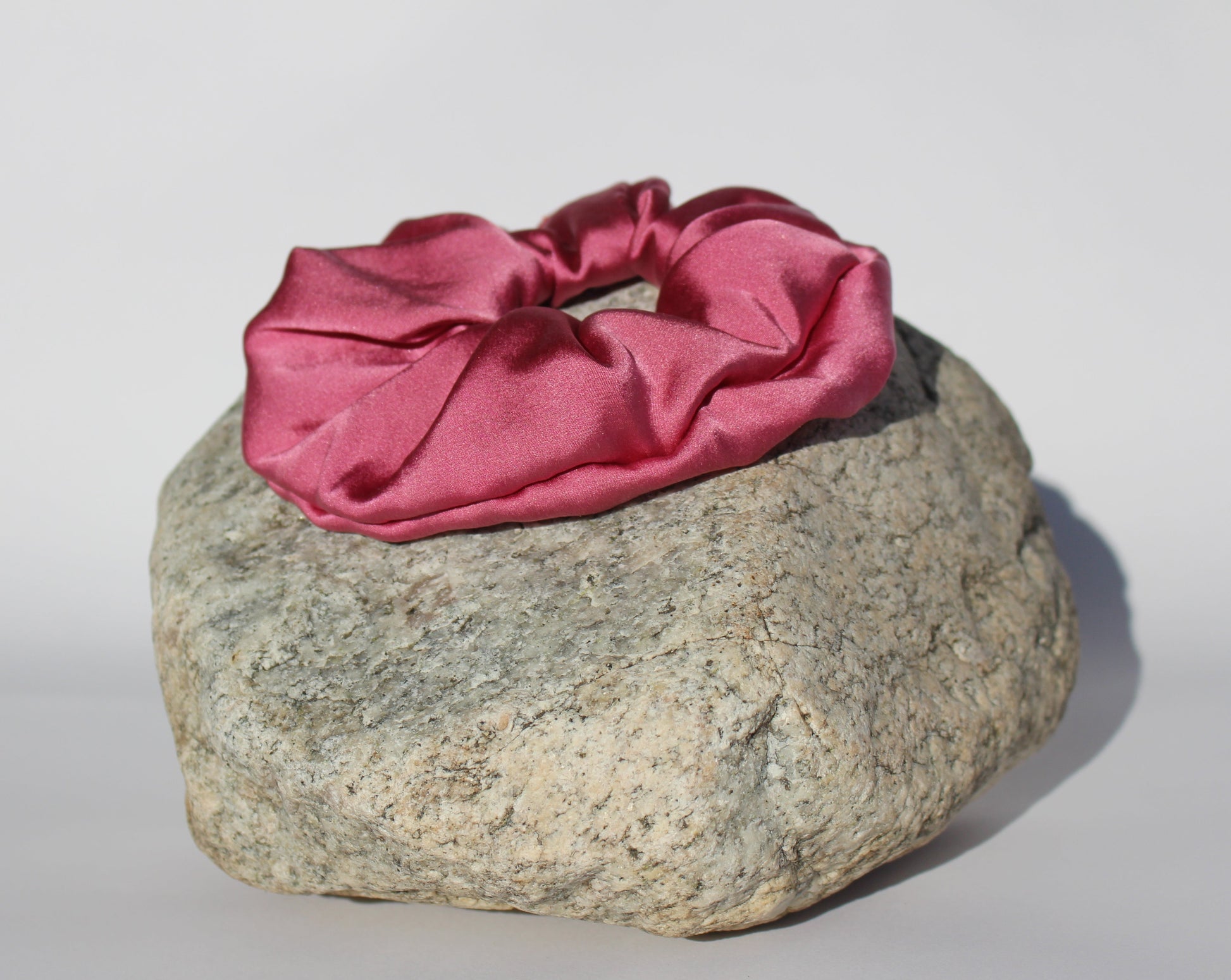 Silk Raspberry colored scrunchie on a rock