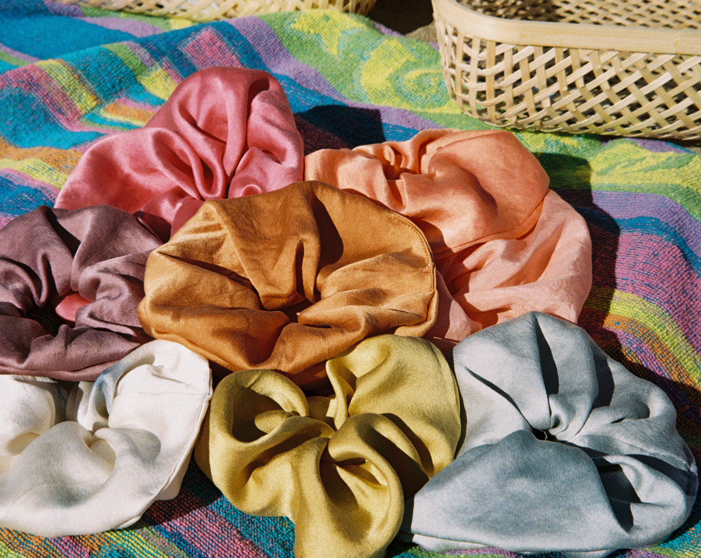 Rainbow Set of silk plant dyed scrunchies on a beach towel on the beach