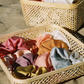 Rainbow Set of silk plant dyed scrunchies in a woven basket on the beach 