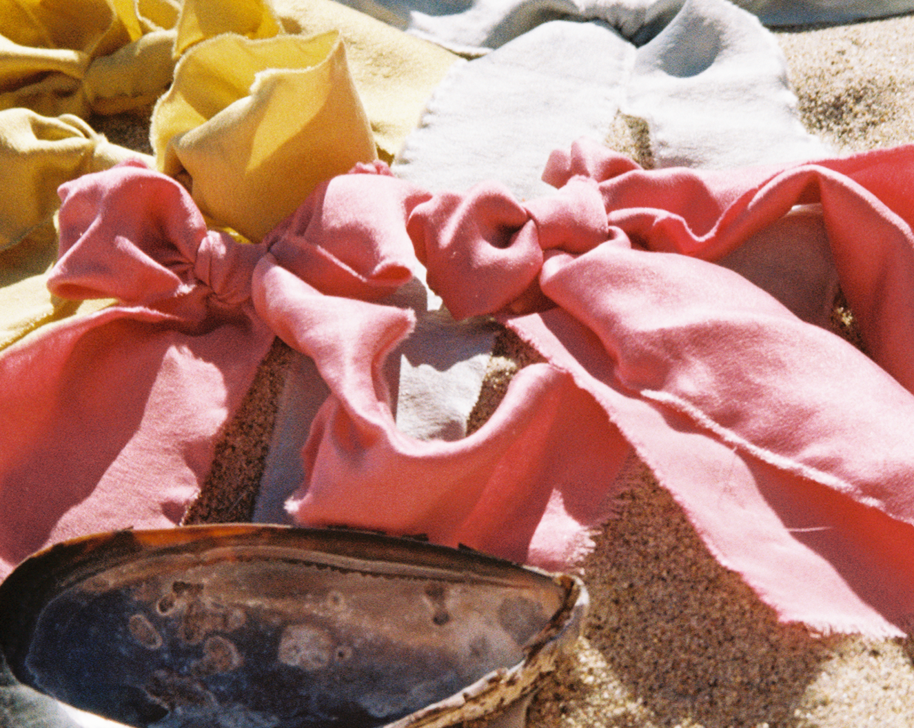 Two Silk pink plant dyed bows are on the beach surround a mussel shell