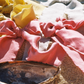 A pair of pink silk scrunchies on the beach next to a mussel shell