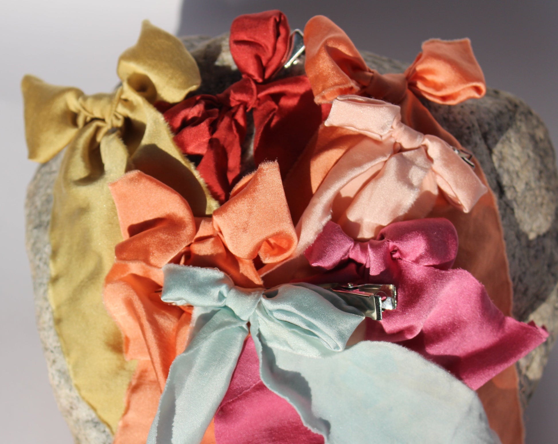 Six silk bows in all different colors laying flat on a rock