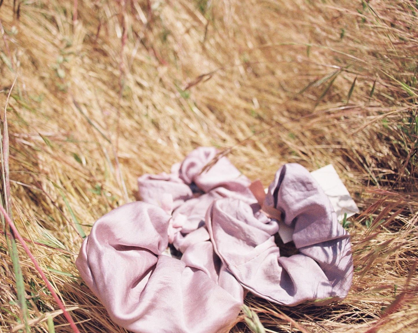 Purple silk scrunchies lay in a field. There are  indigo dyed silk scrunchie. Hand made my Goose Summer Plant Dyes.Goose Summer is a small, sustainable plant dyeing business making naturally dyed silk scrunchies and other accessories in Los Angeles. 