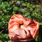 Peach silk scrunchie laying in a bed of clovers