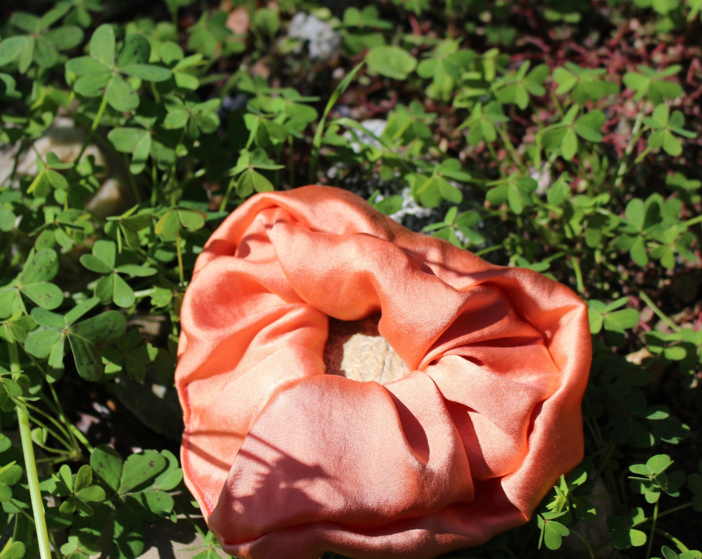 Peach silk scrunchie laying in a bed of clovers