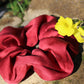 A ruby red silk scrunchie dyed with madder root to make a striking crimson red silk scrunchie, laying on a stone with a yellow flower in the frame