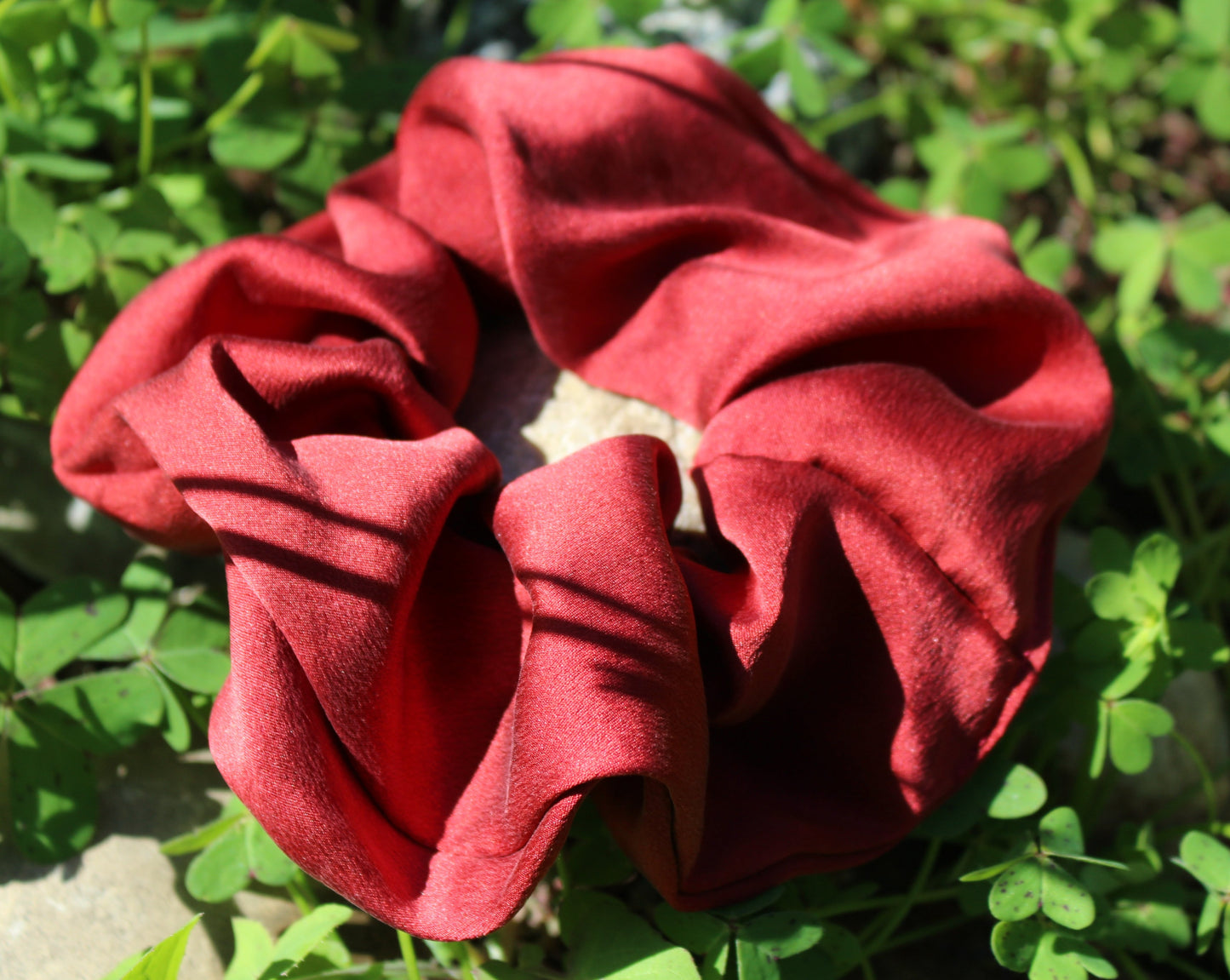 A ruby red silk scrunchie dyed with madder root to make a striking crimson red silk scrunchie, laying in a bed of clovers