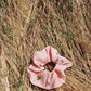 A pink plant dyed silk scrunchie is laying in a field of wheat grass. Hand made my Goose Summer Plant Dyes.Goose Summer is a small, sustainable plant dyeing business making naturally dyed silk scrunchies and other accessories in Los Angeles. 