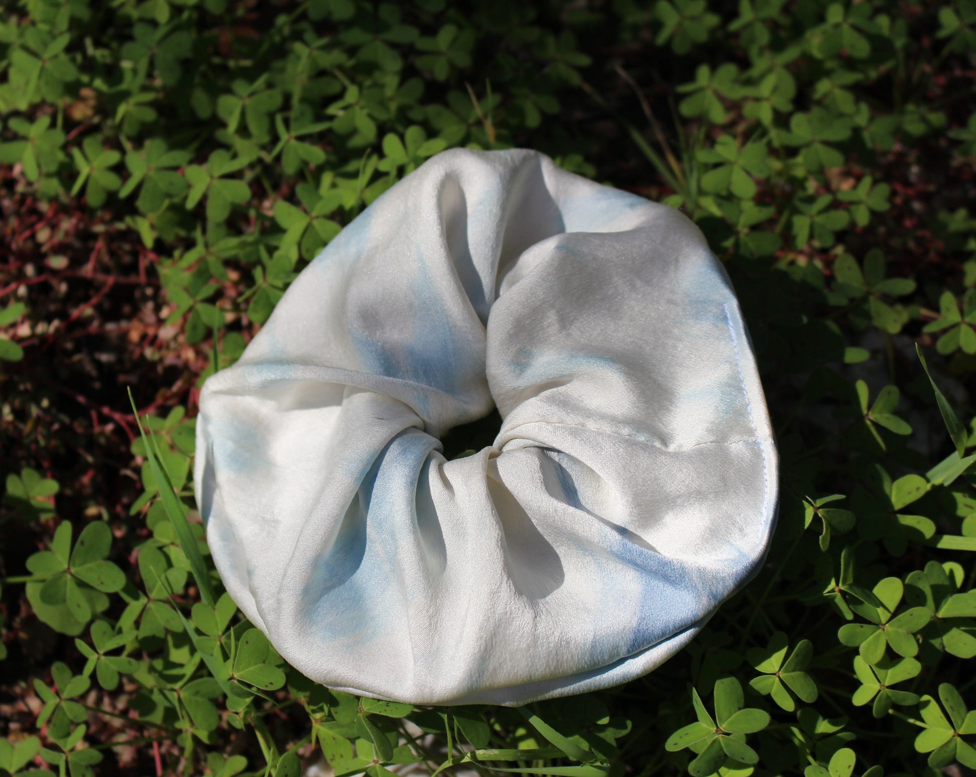 Tie dyed indigo blue and white silk scrunchie lying in a bed of clovers 