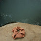 A brownish peach colored silk scrunchie is displayed on a rock. The Sienna Silk Scrunchie sits on a rock beside a hot spring. The Sienna Scrunchie is naturally dyed by Goose Summer with Cutch bark.