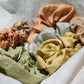 A bundle of assorted naturally dyed silk scrunchies are being displayed. There is a mint green silk scrunchie, light blue silk scrunchie, buttery yellow silk scrunchie, peach and light pink silk scrunchie. All silk scrunchies are naturally dyed.